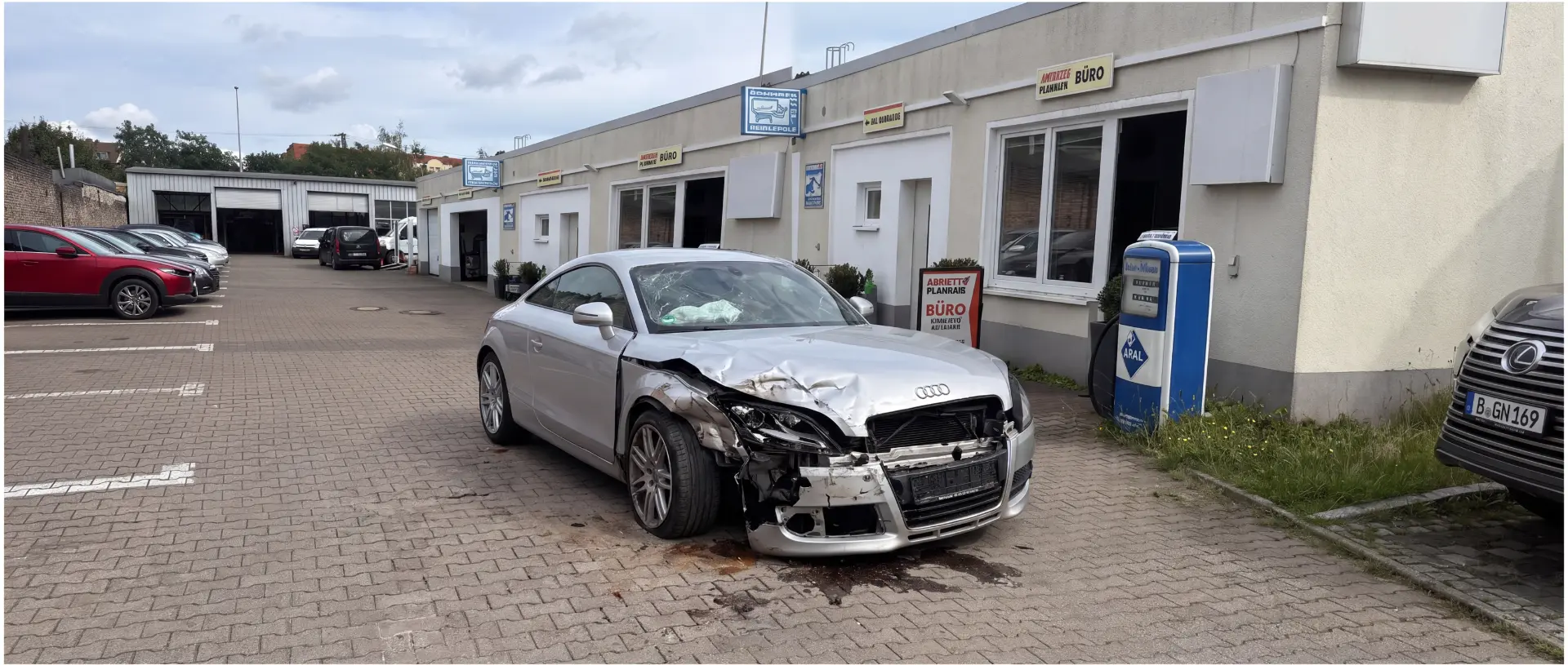 Unfallbeschädigter silberner Audi TT mit Frontschaden vor der Werkstatt bei der Schadenaufnahme